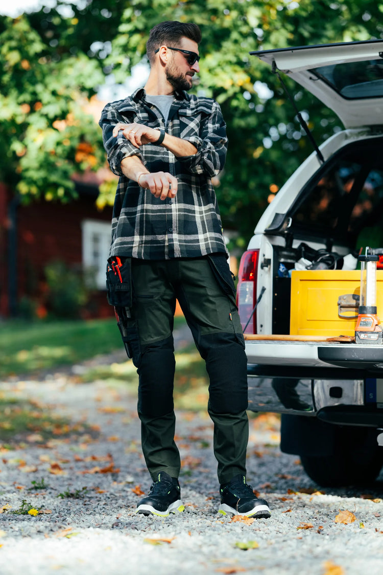 Tradesman in Blåkläder work trousers with holster pockets unloading tools from a pickup