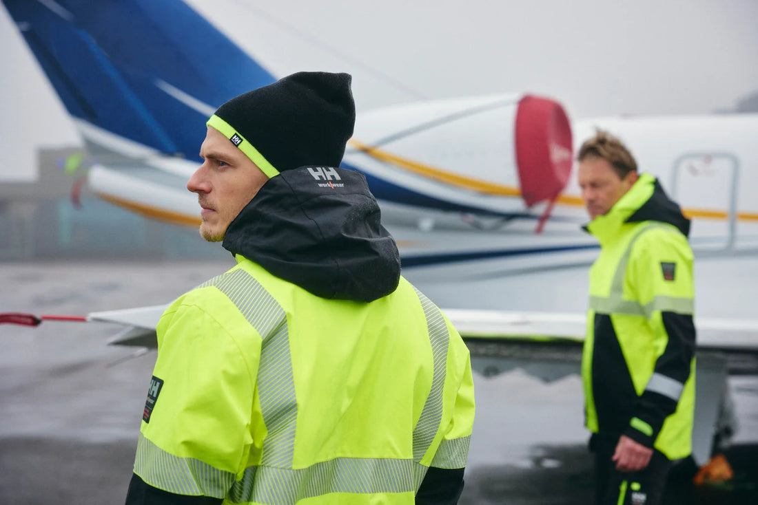 Two workers in Helly Hansen hi-vis rainwear on an airport apron