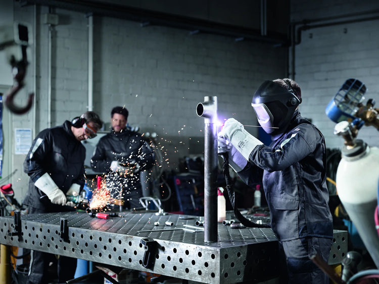 Welders in Kübler workwear and leather welding gauntlets at a workshop bench