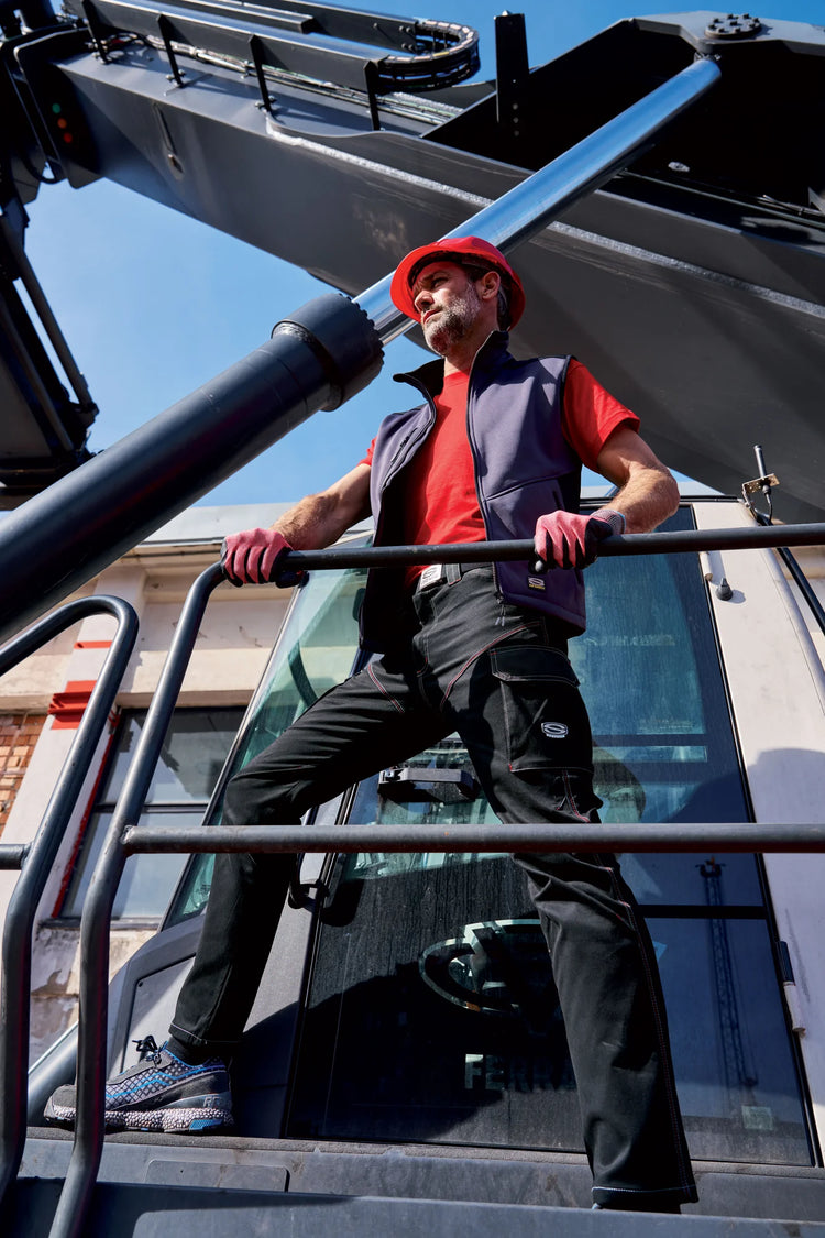 Worker in a Sir Safety bodywarmer and work gloves gripping a machine handrail