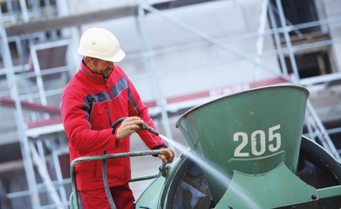 Worker in Planam Plaline workwear and a hard hat cleaning a concrete mixer on a building site